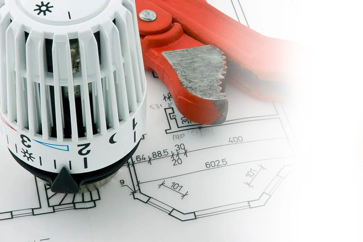 Tête thermostatique et clé serre-tube posées sur un plan de plomberie